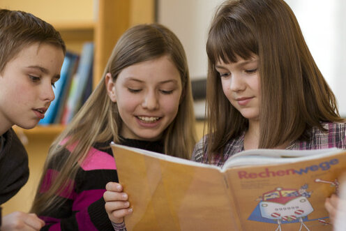 Sachsen: Nachhilfe ist gefragt - Die Grundschüler Lisa-Marie (M.), Benjamin (l.) und Lea (r.) lesen im Nachhilfeunterricht in einem Schulbuch.