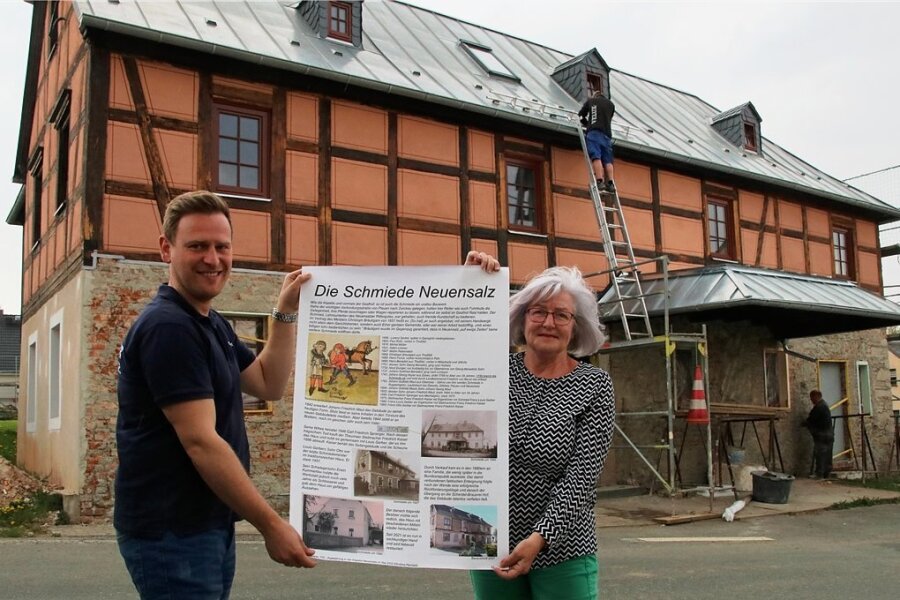 Sandro Klemeth vom Feuerwehrverein und Martina Röber stehen mit dem Ausstellungsplakat zur alten Schmiede vor dem Gebäude, welches der Eigentümer zurzeit sanieren lässt.