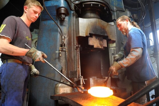 <p class="artikelinhalt">Louis Stasche (links) und Rico Menzel holen das glühende Eisen aus dem Ofen und bearbeiten es mit einem Gesenkhammer. Daraus entstehen soll ein Außenring für ein Kugellager einer großen Maschine. Der Handwerksbetrieb beteiligt sich an der Umweltwoche in Berlin.</p>