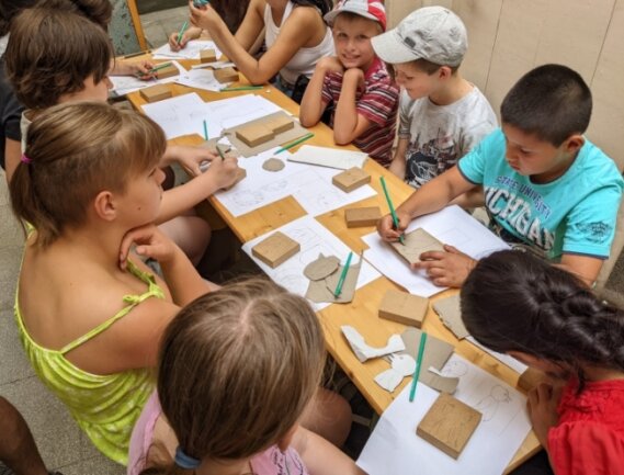 Nachdem die Vorlage auf Papier gezeichnet wurde, übertragen die Kinder die Konturen ihrer Schnitzarbeit auf Holz.