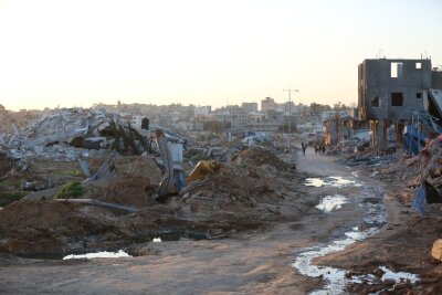 Sechs Monate Gaza-Krieg in Zahlen - Menschen gehen an Trümmern und Ruinen auf einer Straße im Flüchtlingslager Al-Maghazi im Zentrum des Gazastreifens vorbei.