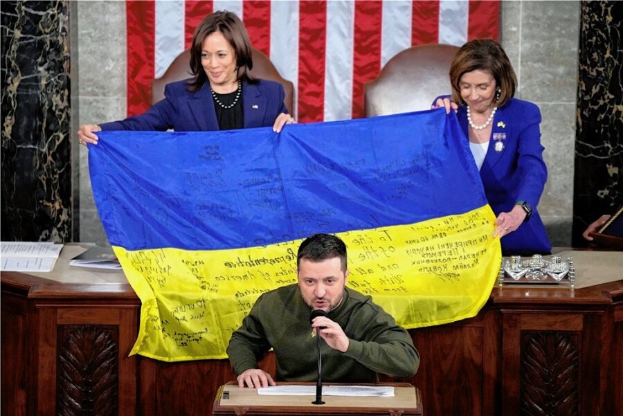 Selenskyj in Washington: "Ich bin sicher, dass wir diesen Krieg gemeinsam gewinnen" - US-Vizepräsidentin Kamala Harris (hinten links) und die Sprecherin des Repräsentantenhauses, Nancy Pelosi, breiten eine von Frontsoldaten signierte ukrainische Flagge aus, während Präsident Wolodymyr Selenskyj zu den US-Abgeordneten spricht. 