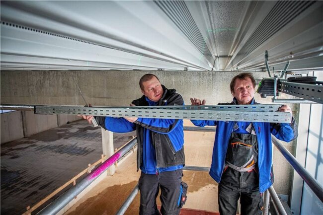 Sporthalle, Digitalisierung der Schule, Umbau im Ärztehaus: Wofür Niederwiesa 2023 Geld ausgibt - In der Sporthalle von Niederwiesa sind die Elektriker zugange. Hier ein Bild von Anfang März: Die Elektrotechniker Lutz Lieberwirth (links) und Andreas Kühnel von der Frankenberger Firma Beyer und Lohs befestigen Kabeltrassen. 