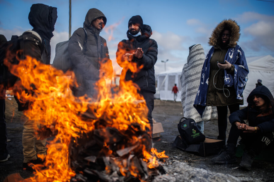 Polen, Medyka: Mehrere Menschen wärmen sich an einem Feuer am Grenzübergang auf.