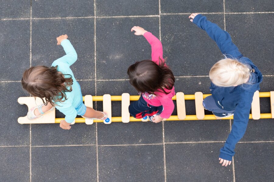 Städtetag fordert mehr Beteiligung an Kita-Finanzierung - Kinder balancieren während eines Pressetermins auf dem Spielplatz einer Kindertagesstätte auf einem Brett.