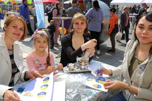 Auf dem Auer Altmarkt wurden am Sonntag auch Anstecker für den Frieden gebastelt. Die kleine Nastja und ihre Mama Ludmilla (l.) sind froh, in Sicherheit zu sein. Jenny Lederer und Lisa-Marie Lorbeer (r.) haben geholfen.