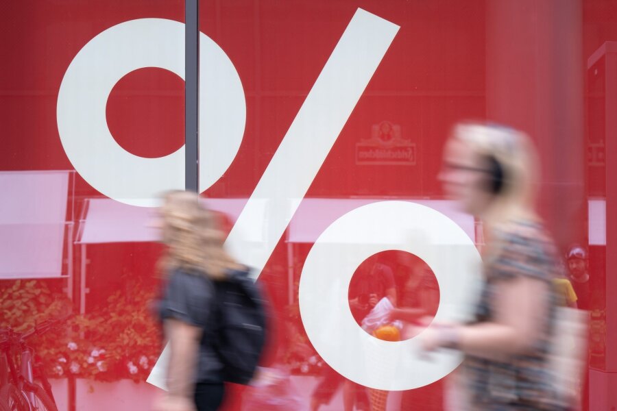 Stimmung ostdeutscher Unternehmen steigt weiter - Passanten gehen in einer Fußgängerzone an einem Schaufenster eines Modegeschäfts vorbei, dass mit einer Rabattaktion wirbt.