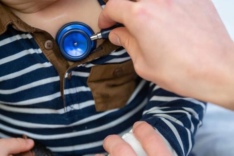            Ein Arzt untersucht ein Kind mit einem Stethoskop. 