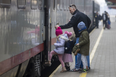 Am Bahnsteig im Bahnhof von Przemaysl warten Flüchtende auf ihre Weiterreise, ein Helfer der polnischen Armee hilft drei Kindern in den Zug.