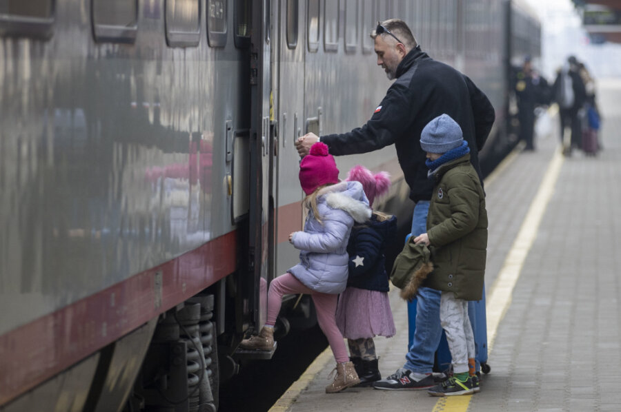 Am Bahnsteig im Bahnhof von Przemaysl warten Flüchtende auf ihre Weiterreise, ein Helfer der polnischen Armee hilft drei Kindern in den Zug.