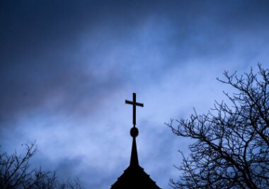 Synode zu Missbrauch und Zukunft in Minderheit - Dunkle Wolken ziehen über das Kreuz auf einer Kirche hinweg.