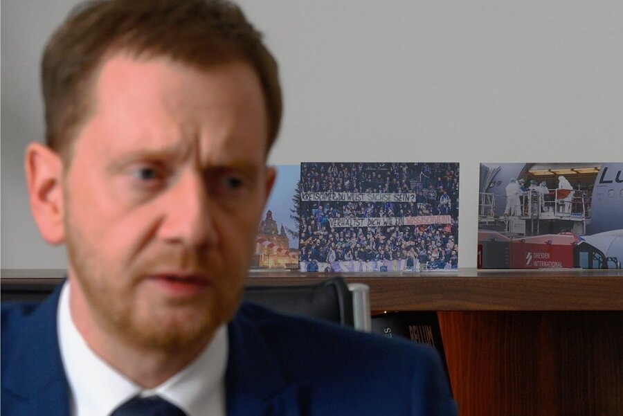 Szenen einer Krise - welche Fotos Kretschmer in seinem Büro an die Pandemie erinnern - Sachsens Ministerpräsident Michael Kretschmer (CDU) beim Interviewtermin vor aufgestellten Fotos mit Szenen der Coronapandemie. 