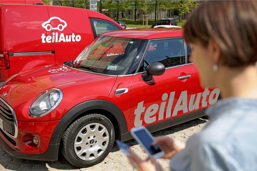 Teilen für mehr Klimaschutz: Bringt Carsharing was für den Umweltschutz? - Eine Frau bucht mit einem Smartphone ein Auto des Anbieters Teilauto auf einem Parkplatz. Das Angebot an Fahrzeugen wächst.