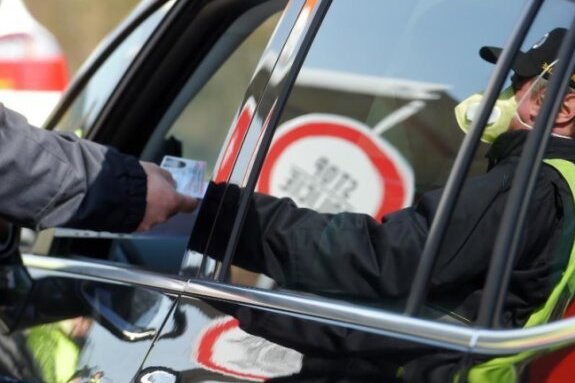 Tschechische Grenzen bleiben wegen Coronavirus monatelang geschlossen - Ein Polizist mit Atemschutzmaske kontrolliert ein Auto an der tschechisch-deutschen Grenze. 