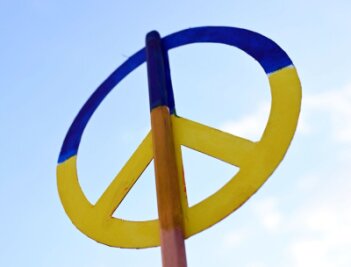 Bei einer Mahnwache zum Ukraine Krieg wird ein Friedenssymbol in den Farben der Ukraine in den Himmel gehalten.