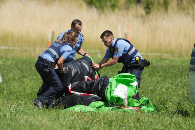Polizeibeamte transportieren die Hülle einer Hüpfburg ab. Das Spielgerät war bei einem Fest auf dem Sportplatz von Gondershausen von einer Windböe erfasst und mindestens vier Meter in die Höhe gehoben worden.
