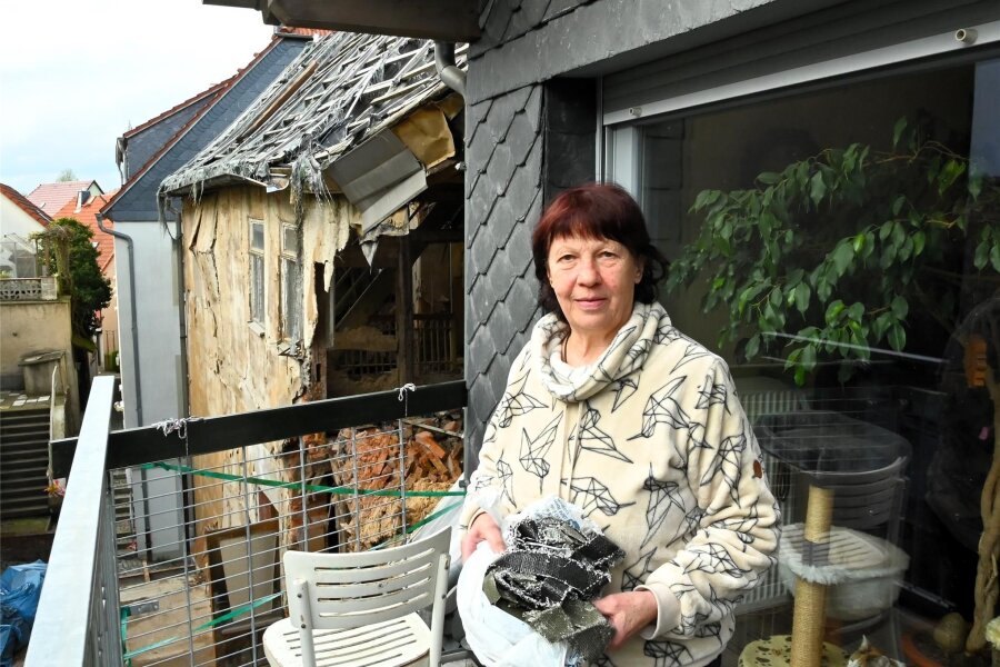 Vermieterin in Hainichen in Angst: „Mein Nachbarhaus fällt zusammen“ - Petra Haertel steht auf ihrem Balkon in der Marktstraße 5 in Hainichen, hinter ihr das halb abgerissene Nachbarhaus. In der Hand hält sie die Reste der alten Dachabdeckung, die sie weiterhin auf ihrem Grundstück findet.