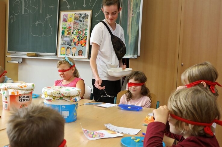 Der Freiwilligendienstleistende Antony Peger verteilt an Kinder der Grundschule in Langenberg bei einem Projekt Früchte. Mit verbundenen Augen sollen diese gekostet und so erkannt werden. 