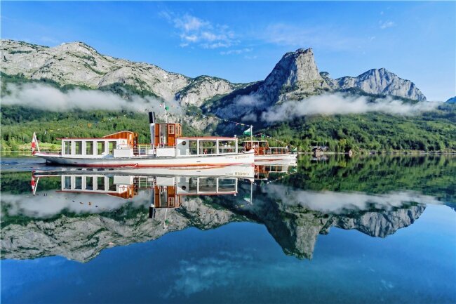 Von See zu See: Eine Tour durch das steirische Salzkammergut - Das MS "Rudolf" (vorn) ist eines von drei Schiffen, die auf dem Grundlsee unterwegs sind. 1903 gefertigt, wurde es mehrfach modernisiert und erhielt 2017 einen umweltfreundlicheren diesel-elektrischen Antrieb. Acht naturbelassene Badestrände findet man rund um den See, der im Sommer bis zu 23 Grad warm wird. 