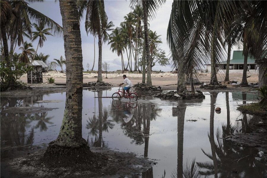 Vor dem Untergang - Nach dem Sturm ist vor dem Sturm: Ein Junge radelt über ein geflutetes Gelände eines Atolls, das zu Tuvalu in der Südsee gehört. Das Wasser holt sich immer mehr Land. Manche der alten Kokospalmen könnten beim nächsten Unwetter ein Opfer des Meeres werden.