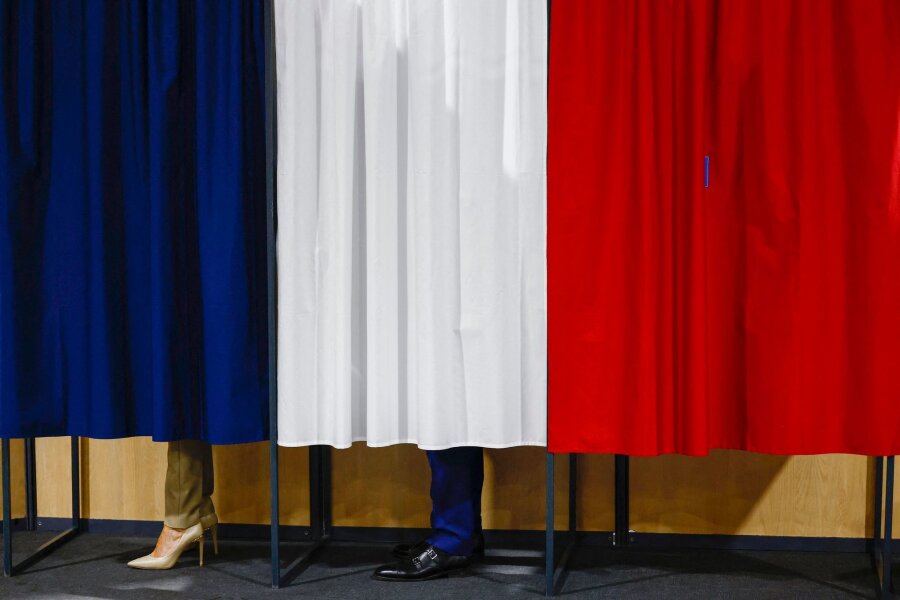 Wahl in Frankreich: Rechtsnationale bei erster Runde vorne - Der französische Präsident Emmanuel Macron und seine Frau Brigitte Macron stehen vor der Stimmabgabe in der Wahlkabine.