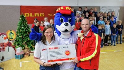 Warum Lebensretter eine Glauchauer Schule auszeichnen - Lehrerin Anja Haberkorn und DLRG-Landespräsident Andreas Lorenczat freuen sich mit Maskottchen Nobbi über den Förderpreis.