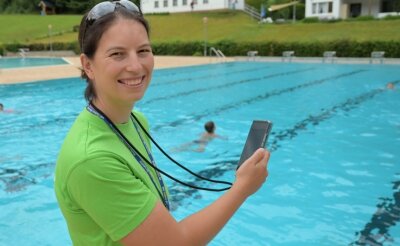 Warum Schulkinder ins Freibad gehen - Anne Arnold steht mit der Stoppuhr auf den Handy am Beckenrand und misst die erworbene Ausdauer von Grundschülern beim Schwimmen.