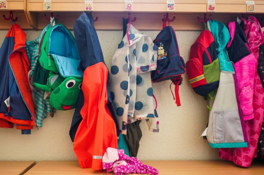 Symbolbild: Jacken und Rucksäcke hängen in der Garderobe einer Kita. Ab Dienstag dürfen berufstätige Eltern in Sachsen ihre Kinder wieder zur Kita bringen. 