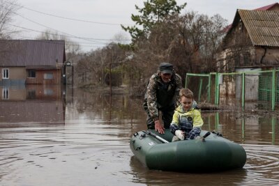 Wasser in russischem Flutgebiet steigt weiter stark an - Ein Mann schiebt ein Schlauchboot mit einem Jungen in einem überfluteten Gebiet in Orenburg, Russland.