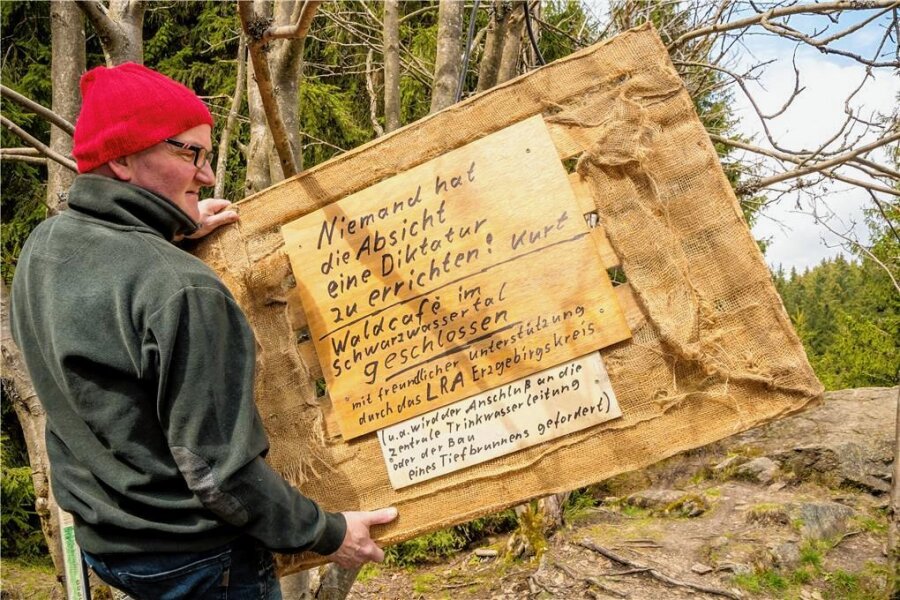 Wegen EU-Recht: Muss Kaffee-Kurt sein Waldcafé im Erzgebirge dicht machen? - In einem Baum, der direkt an der Stelle steht, an der er sonst das Waldcafé zu finden ist, hängt Kaffee-Kurt ein Schild auf, mit dem er über die aktuelle Situation aus seiner Sicht informiert. 