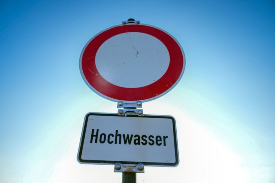 Weniger Unwetterschäden als befürchtet in Sachsen - Ein Verkehrsschild für "Durchfahrt verboten" mit dem Zusatz "Hochwasser" steht am Ufer eines Flusses.