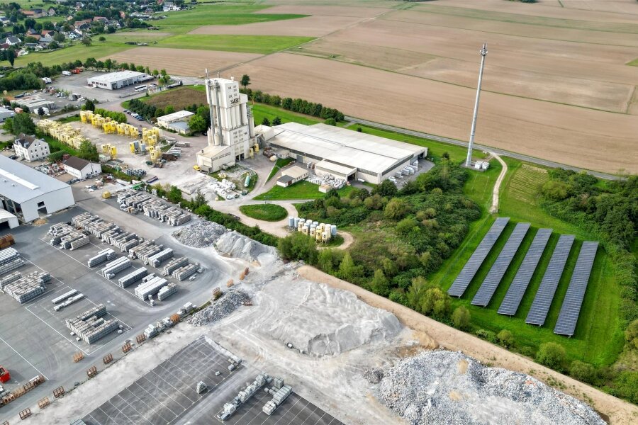 Wie ein Baustoffhersteller durch die Krise kommt - Ein Drohnenbild gibt einen Überblick über das Firmengelände Sakret in Diethensdorf mit markantem Turm, Fotovoltaikanlage und vielen Grünflächen.