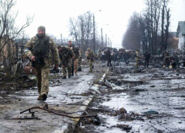 Ukrainische Soldaten inspizieren die Trümmer einer zerstörten russischen Panzerkolonne auf einer Straße in Butscha.