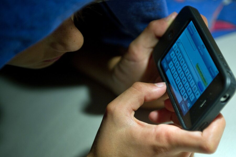 Wie Kinder weniger Zeit vor Bildschirmen verbringen - Ein elfjähriger Junge liegt unter der Bettdecke und schreibt auf einem Smartphone eine SMS. Kinder unter 13 Jahren sollten Experten zufolge keinen Zugang zu derartigen Medien haben.
