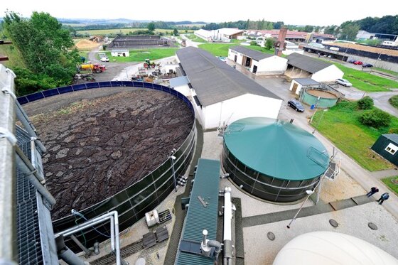 Wie wird aus Biogas Strom und Wärme produziert? - Blick auf den Behälter für Rest-Gülle (links), den Container mit dem Generator (Mitte) und auf Zwischenspeicher
