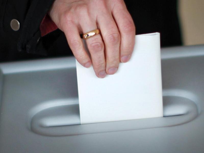 Eine Person wirft in einem Wahllokal den Stimmzettel in eine Wahlurne.